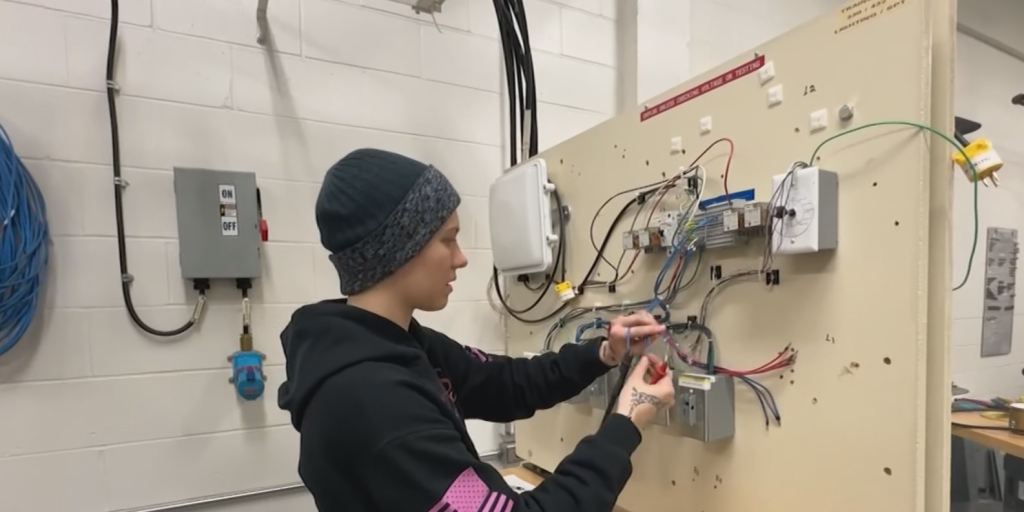 Kelsey Johannsen working on electrical connections. Image features a MELTRIC receptacle in the background.